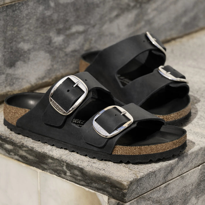 Black sandals with silver buckles on a stone surface