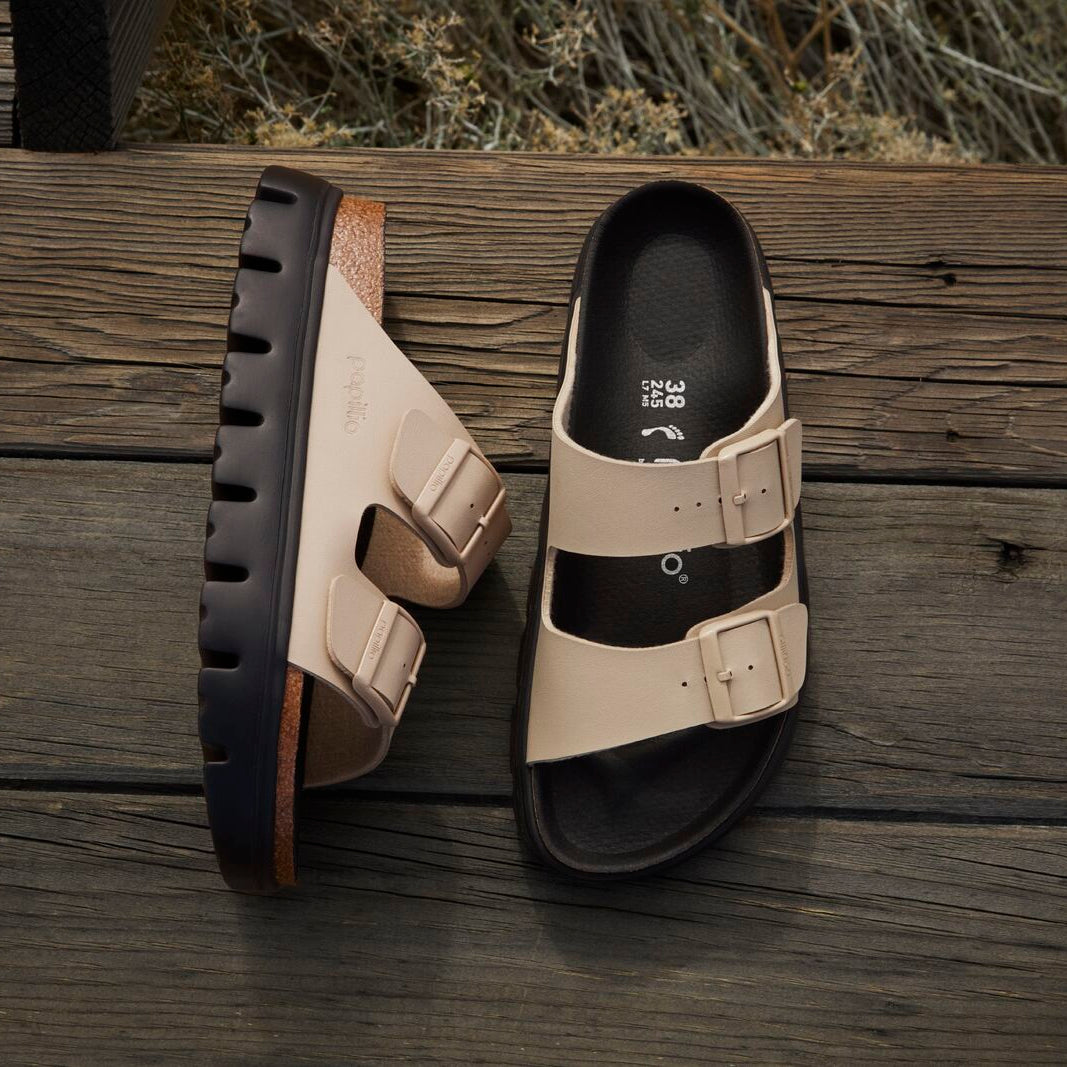 Pair of beige sandals with black soles on a wooden surface