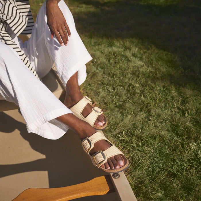 Person wearing white sandals sitting on a step with grass in the background