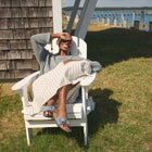 Person lounging on a white Adirondack chair by a wooden cabin with a view of the water.