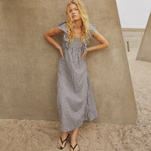 Woman in a checkered dress standing against a textured wall.