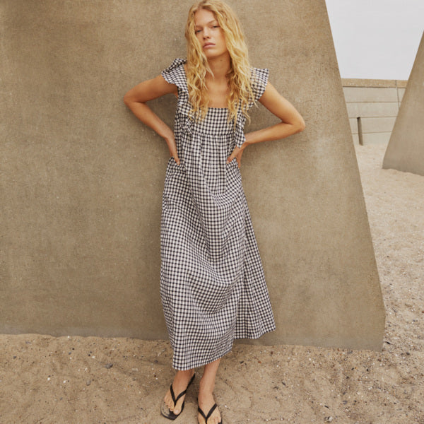 Woman in a checkered dress standing against a textured wall.