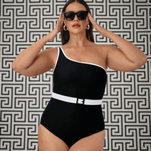 Woman wearing a black one-shoulder swimsuit with a white belt against a geometric patterned wall.