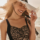 Woman in a black and white patterned dress and straw hat on a beach
