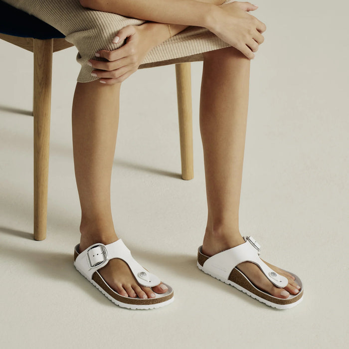 Person wearing white sandals sitting on a chair with a neutral background