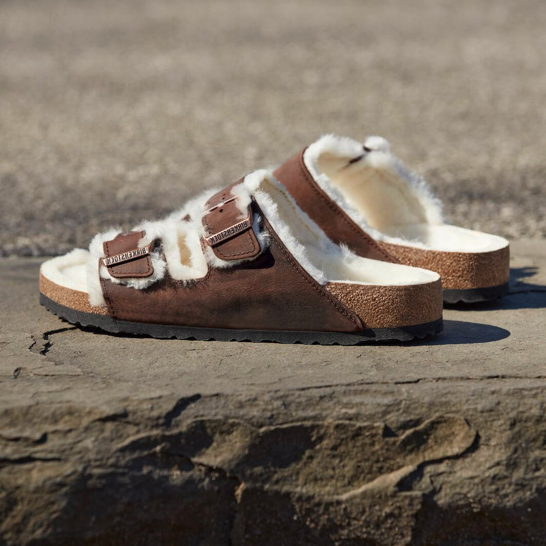Brown sandals with fur lining on a stone surface